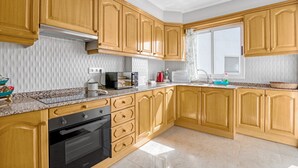 Una cocina con armarios de madera, horno empotrado y ventana con cortinas.