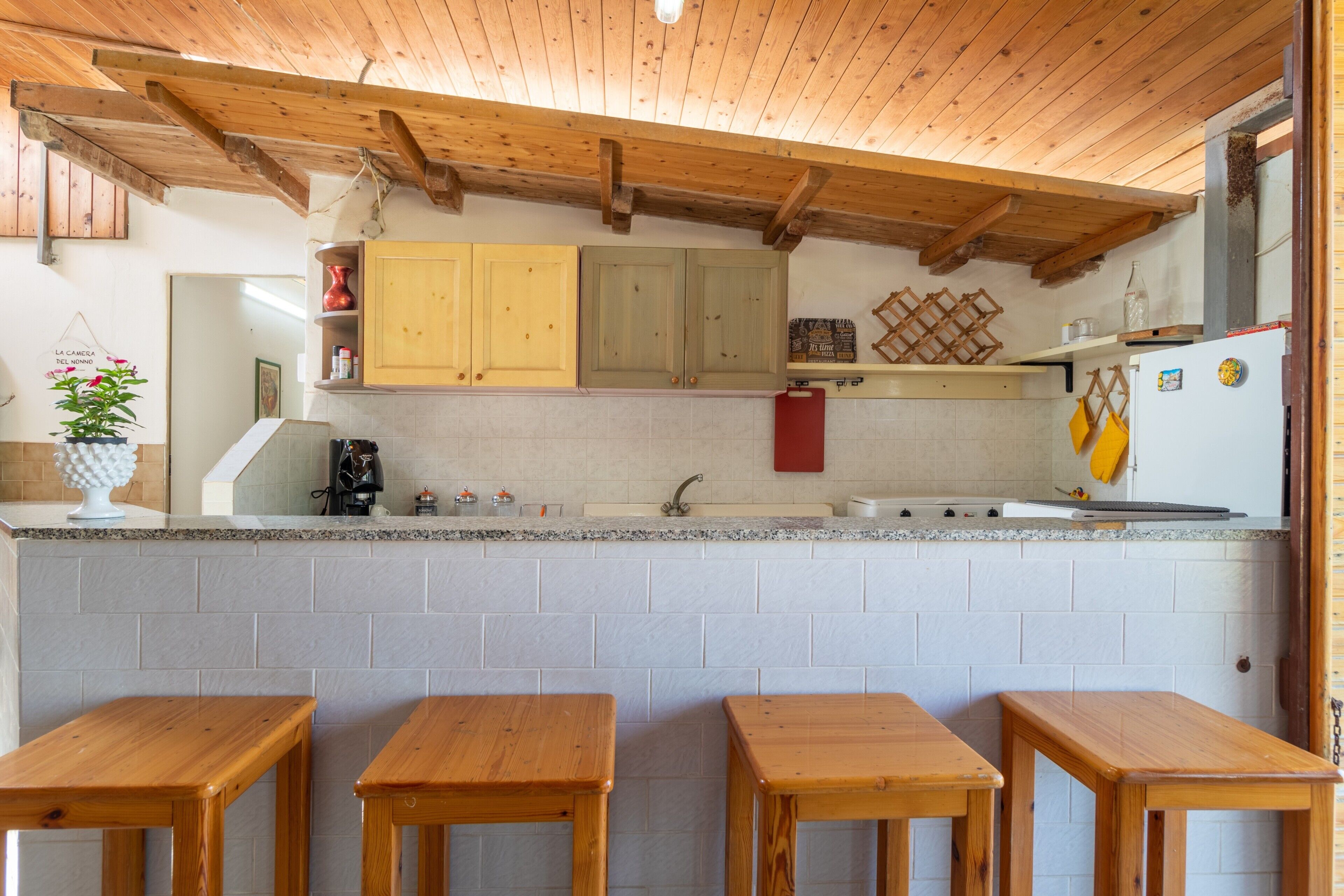 Une cuisine avec des meubles en bois, un plan de travail en granit et quatre tabourets en bois.