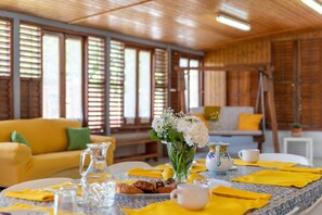 A dining area with a table set for breakfast, a vase with flowers, and a wooden ceiling.