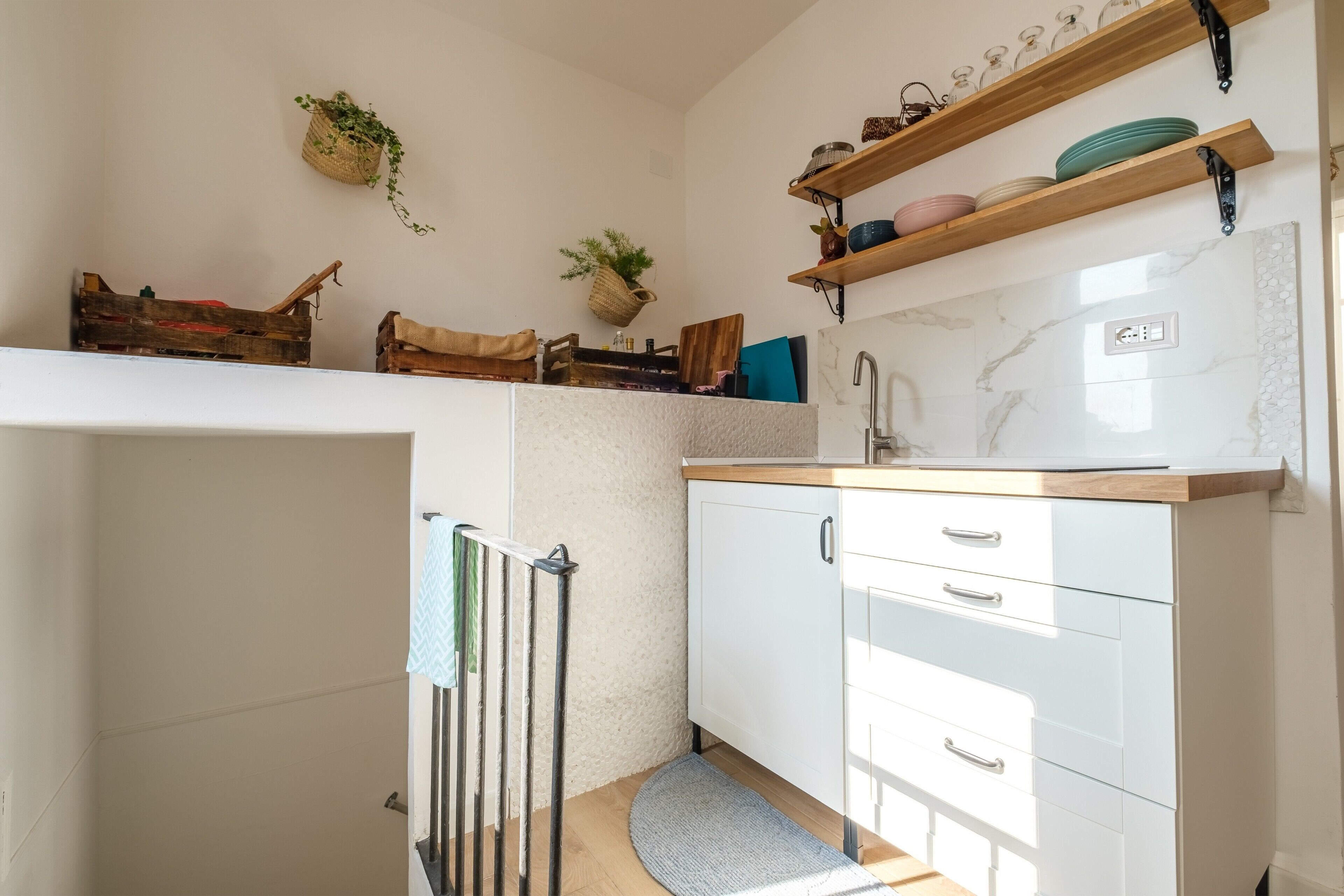 A kitchen with white cabinets, a wooden countertop, and a hanging plant.