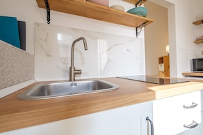 Une cuisine dotée d’un évier en acier inoxydable, d’un plan de travail en bois, de meubles blancs et d’un pare-feu en marbre.