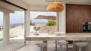 Una cocina moderna con una isla grande, taburetes de bar, una lámpara colgante y vistas al exterior.