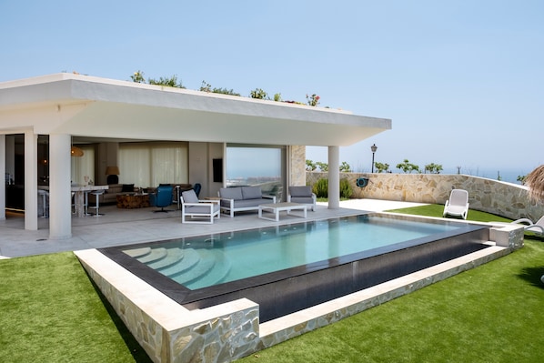 A modern outdoor pool area with a covered seating area, stone walls, and a view of the landscape.