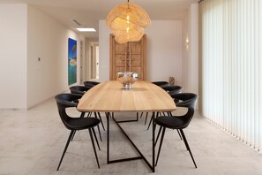 A modern dining area with a wooden table, black chairs, a central bowl, and a woven light fixture.