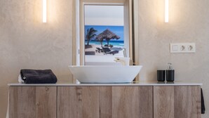 Ein Badezimmer mit einem Holzwaschtisch, einem weißen Waschbecken, einem Handtuch und einem Spiegel mit Strandmotiv.