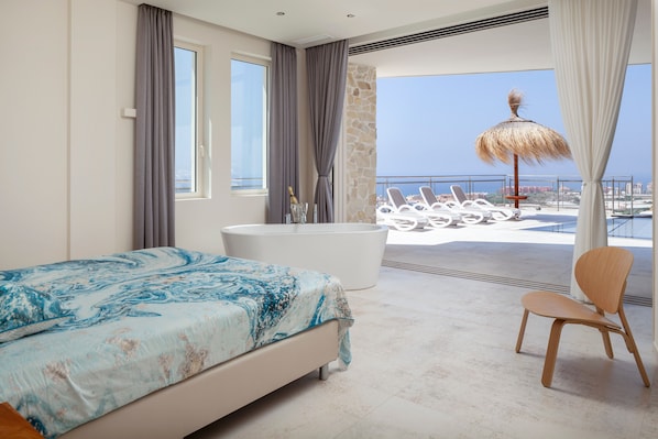 A bedroom with a large bed, a bathtub, and a view of the sea.