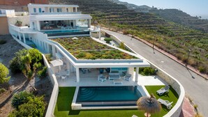 Ein modernes, zweistöckiges Haus mit Swimmingpool, Sitzgelegenheiten im Freien und Blick auf die umliegende Landschaft.