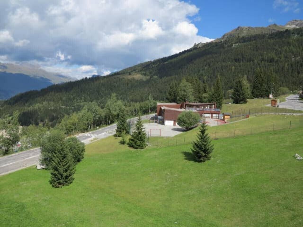 A building with a red roof, surrounded by a fenced area with green grass and trees.
