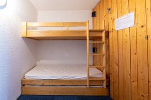 Una cama litera con escalera de madera, colchón blanco y pared de madera con una puerta y un aviso.