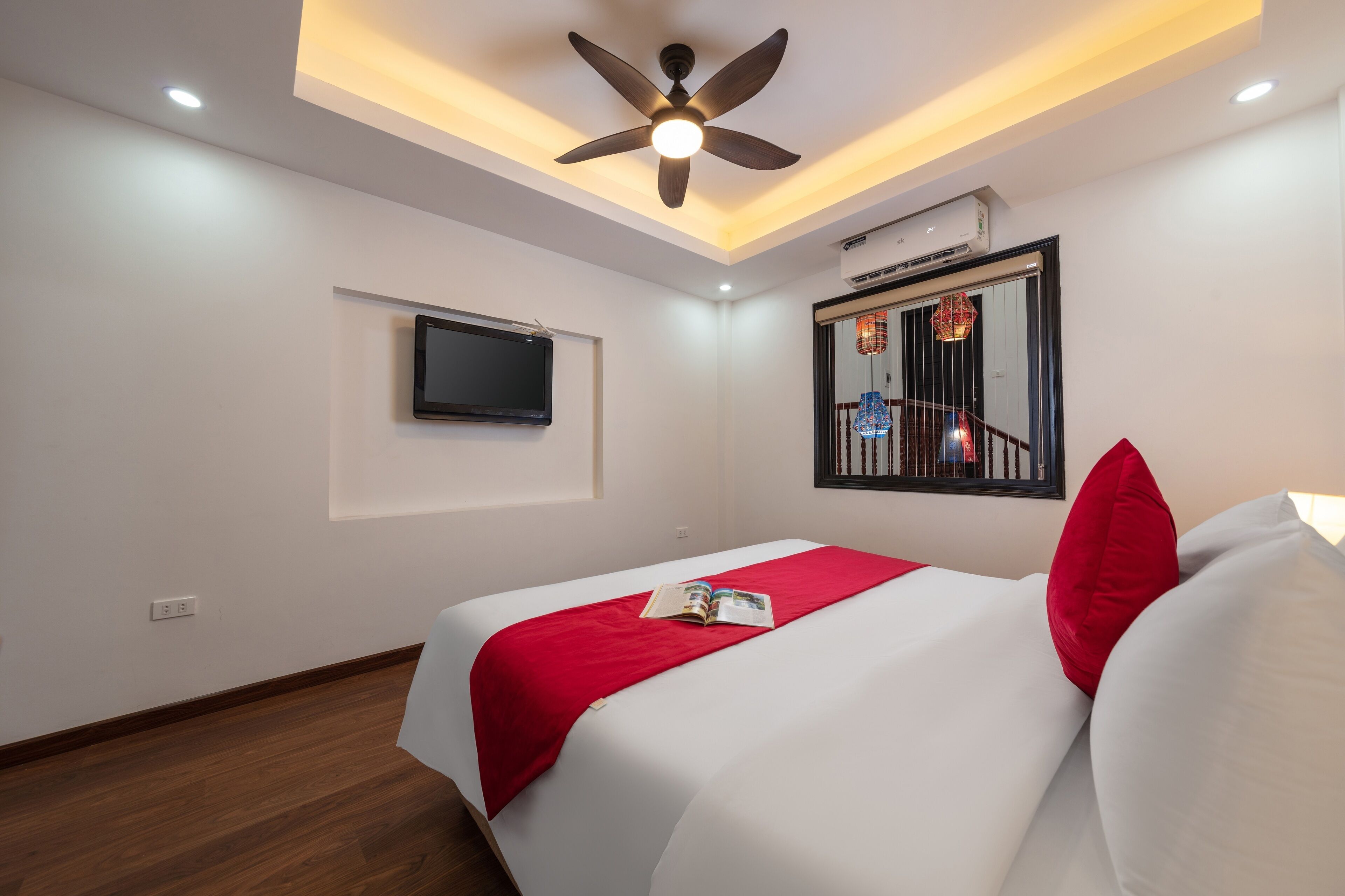 Habitación de hotel con cama, ventilador de techo, televisor montado y ventana con vista a un balcón.