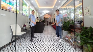 A hotel reception area with a patterned floor, a reception desk, and a staircase in the background. - Hanoi Liliane Hotel and Travel (Hanoi)
