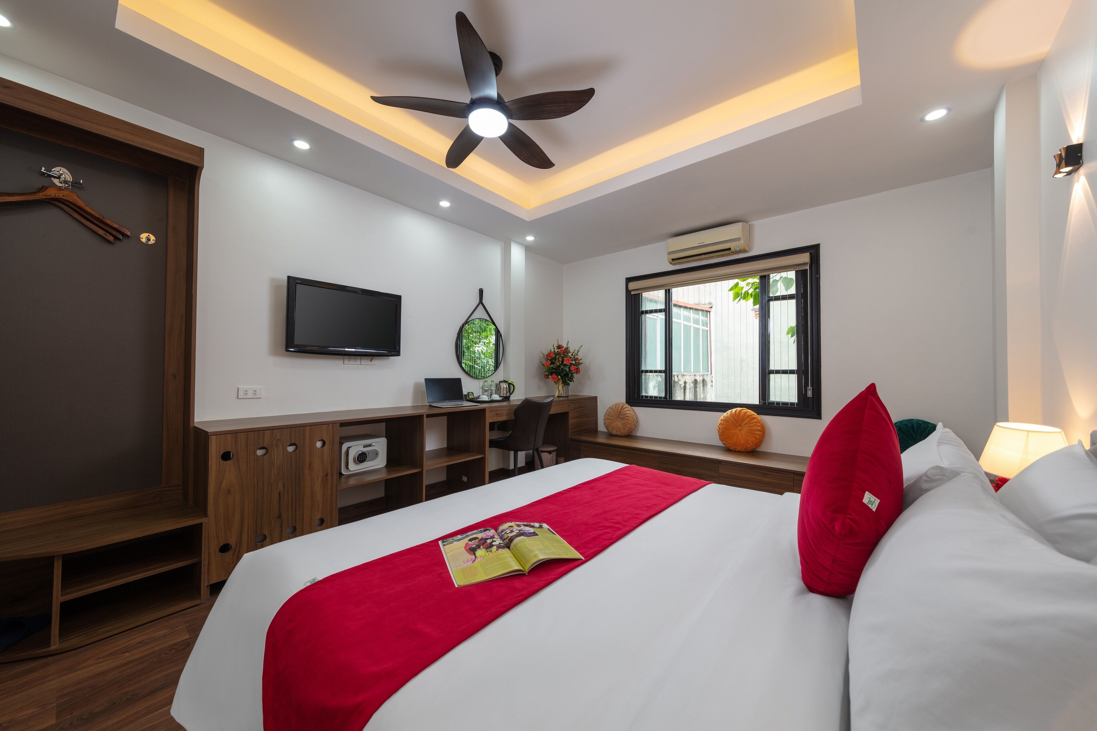 A modern hotel room with a bed, a desk, a TV, and a ceiling fan.