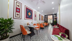 A modern dining area with geometric patterned flooring, orange chairs, and a red sofa. - Hanoi Liliane Hotel and Travel (Hanoi)