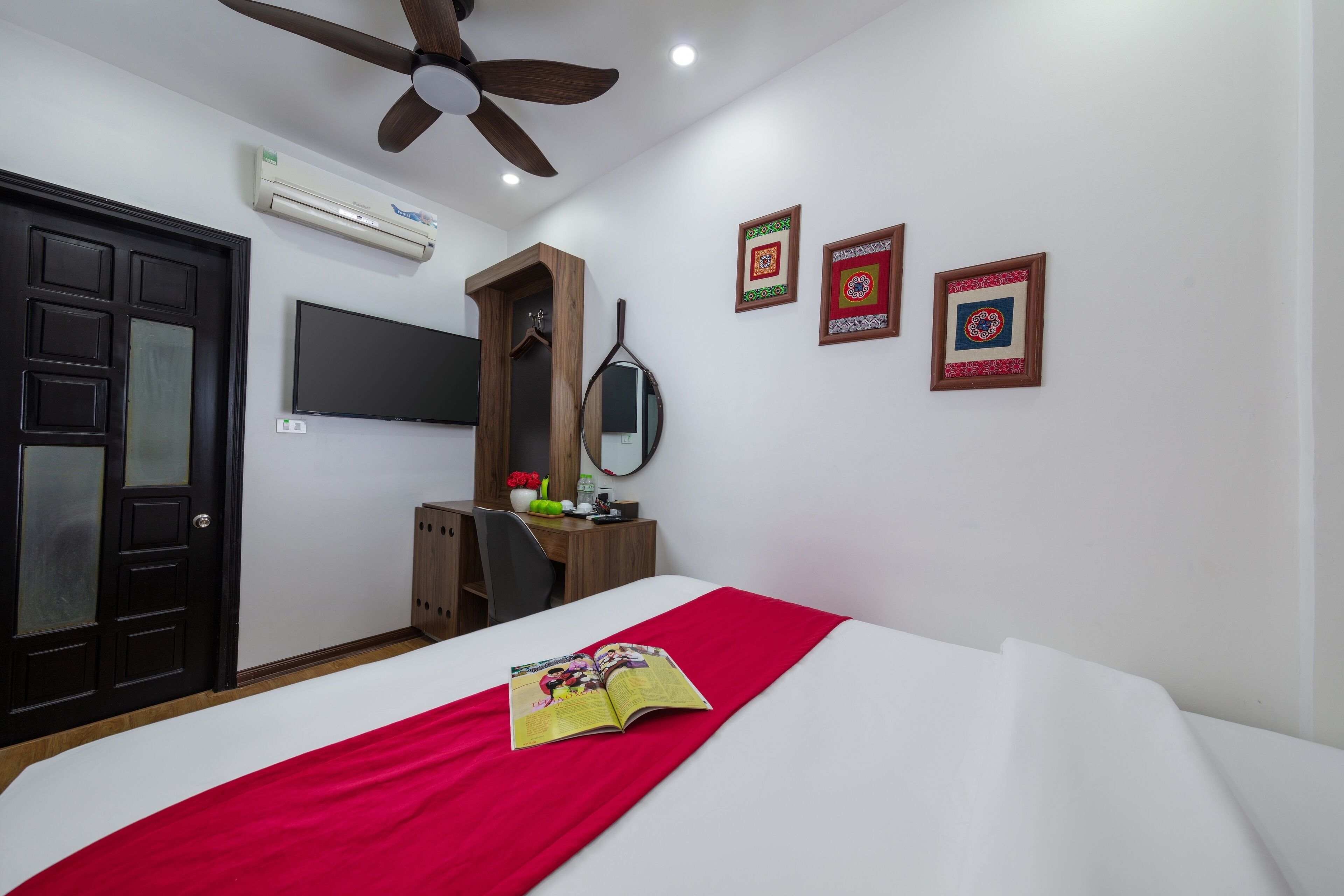 A bedroom with a bed, a ceiling fan, a TV, a desk with a chair, and a wardrobe.