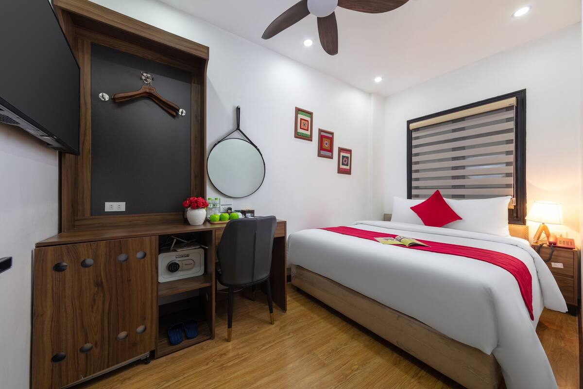 Een hotelkamer met een bed, bureau, stoel, kledingkast en een plafondventilator.