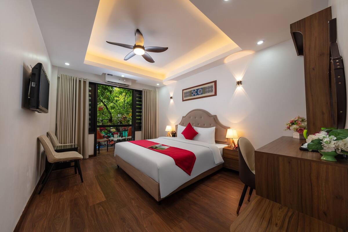 Een moderne hotelkamer met een groot bed, een bureau, een stoel en een plafondventilator.