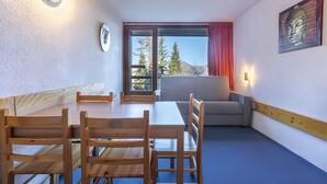 Une pièce comprenant une table à manger en bois, des chaises, un canapé, une fenêtre donnant sur des arbres et des montagnes, et un tableau représentant un Bouddha accroché au mur.