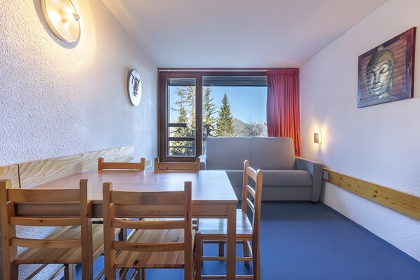 Una habitación con una mesa de comedor de madera, sillas, un sofá, un ventanal con vistas a árboles y montañas, y un cuadro de Buda en la pared.
