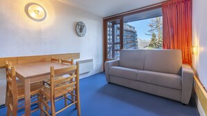 Une pièce comprenant une table à manger et des chaises, un canapé, une fenêtre avec des rideaux et une horloge fixée au mur.
