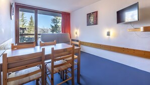 Une pièce comprenant une table à manger, des chaises, un téléviseur fixé au mur et une fenêtre avec des rideaux.