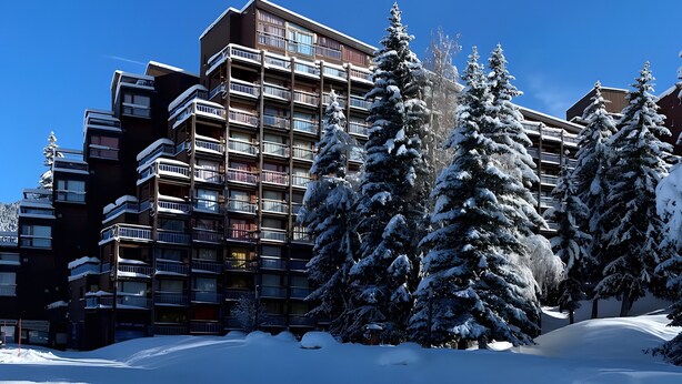 Un paysage enneigé avec un immeuble à plusieurs étages doté de balcons et d’arbres chargés de neige.