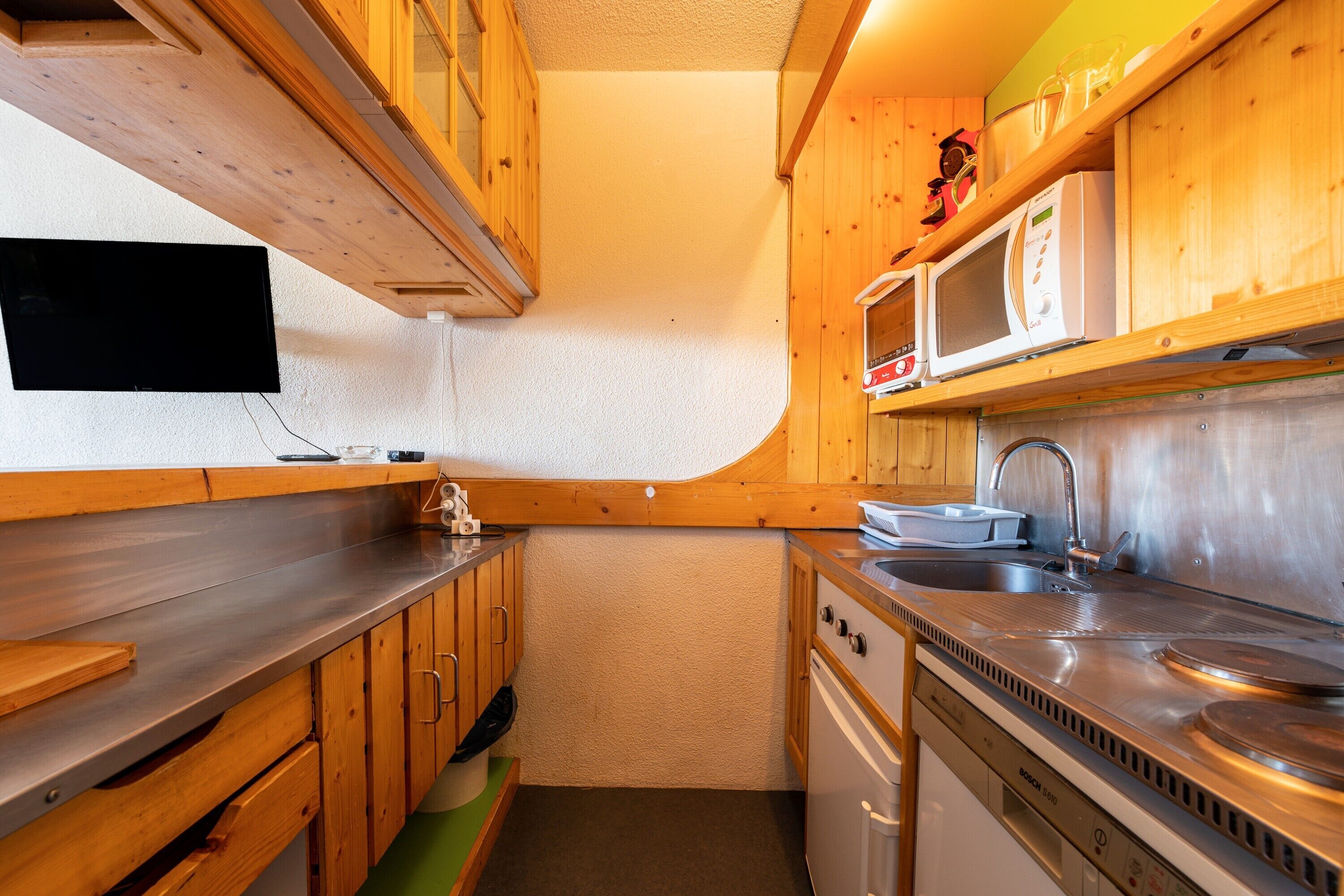 A compact kitchen with wooden cabinets, a stainless steel sink, and a microwave.