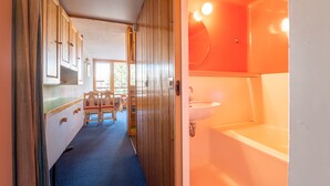 Un couloir étroit mène à une salle de bain équipée d’un lavabo et d’une baignoire.
