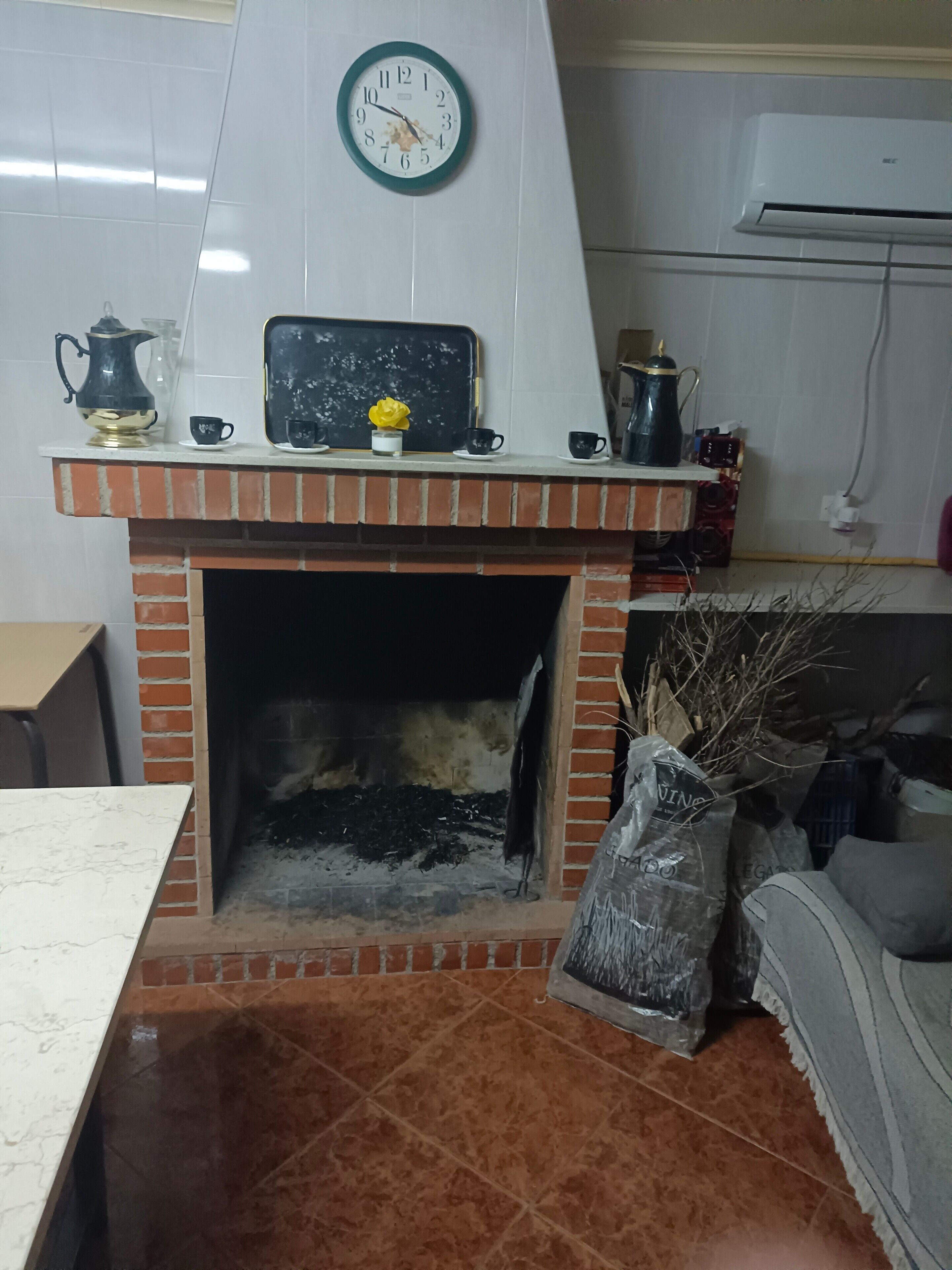 A kitchen with a brick fireplace, a clock, and various kitchen items on the counter.