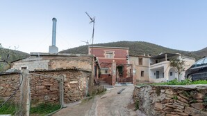 Paesaggio rurale con un muro di pietra, un edificio con un camino e un'auto nelle vicinanze.