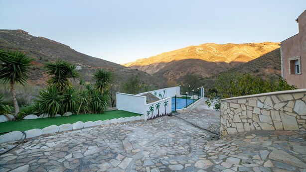 Un cortile lastricato in pietra con piscina, palme e montagne sullo sfondo.