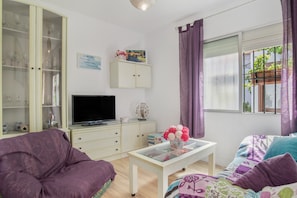 Een woonkamer met een bank, een salontafel, een televisie, een kast en een raam met gordijnen.