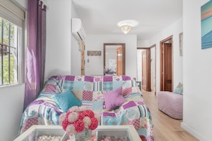 Een kamer met een kleurrijk patchworkbed, een houten vloer, een witte muur en een deur naar een andere kamer.