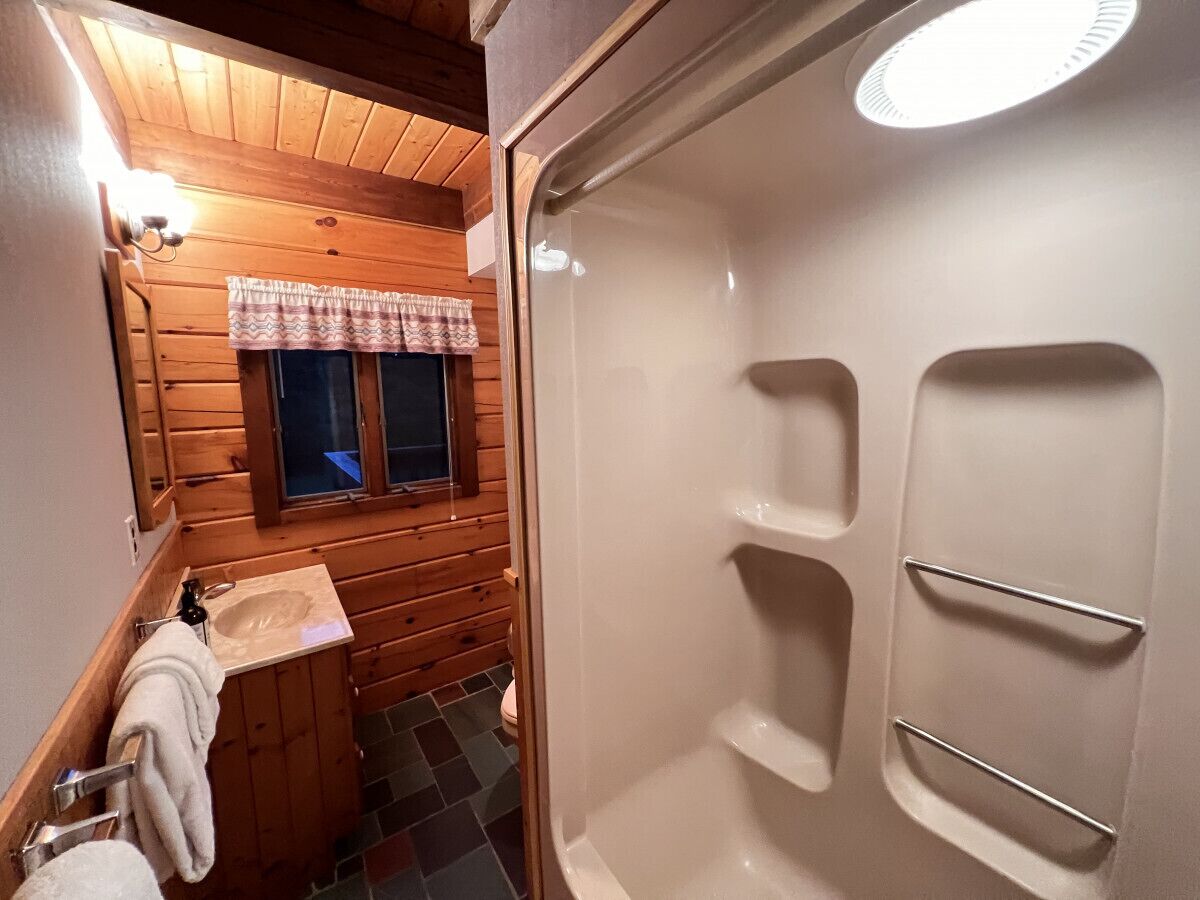 A compact bathroom with a wooden interior, a sink, a mirror, and a shower area.