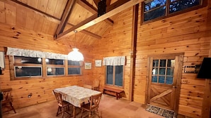 Interior de uma cabana de madeira com uma mesa de jantar, cadeiras, um banco e uma porta com janelas.