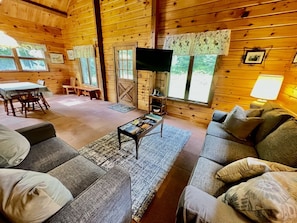 A cozy cabin interior with a sofa, coffee table, and a TV mounted on the wall.