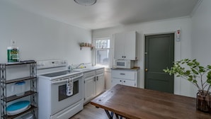 A compact kitchen with white cabinets, a stove, microwave, and a wooden table. - K's Motel - Fishermans Retreat - Cottage (Clayton)