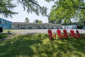 Un motel avec une rangée de chaises rouges sur la pelouse devant et un bâtiment doté de nombreuses fenêtres et d’un toit plat.