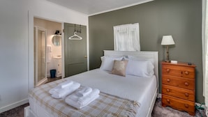 A neatly arranged bedroom with a bed, a dresser, a mirror, and a door leading to a bathroom. - K's Motel - Fishermans Retreat - Cottage (Clayton)