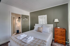 Une chambre à coucher bien rangée, avec un lit, une commode, un miroir et une porte donnant sur une salle de bain.