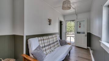 A room with a sofa, a wicker chair, a basket, and a hanging light fixture.