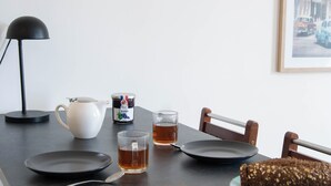 En frukostuppdukning med croissanter, ett bröd, en tekanna, ett glas te och en burk marmelad på ett bord.