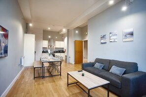 Una sala de estar moderna con un sofá, una mesa de centro, una mesa de comedor y sillas. Se observa una cocina al fondo con armarios y un refrigerador.