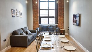 A modern living room with a dining table set for six, a sofa, and a large window with a view. - The Onyx Suite Summar (Manchester)