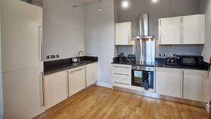 A modern kitchen with white cabinets, a black countertop, stainless steel appliances, and a wooden floor. - The Onyx Suite Summar (Manchester)