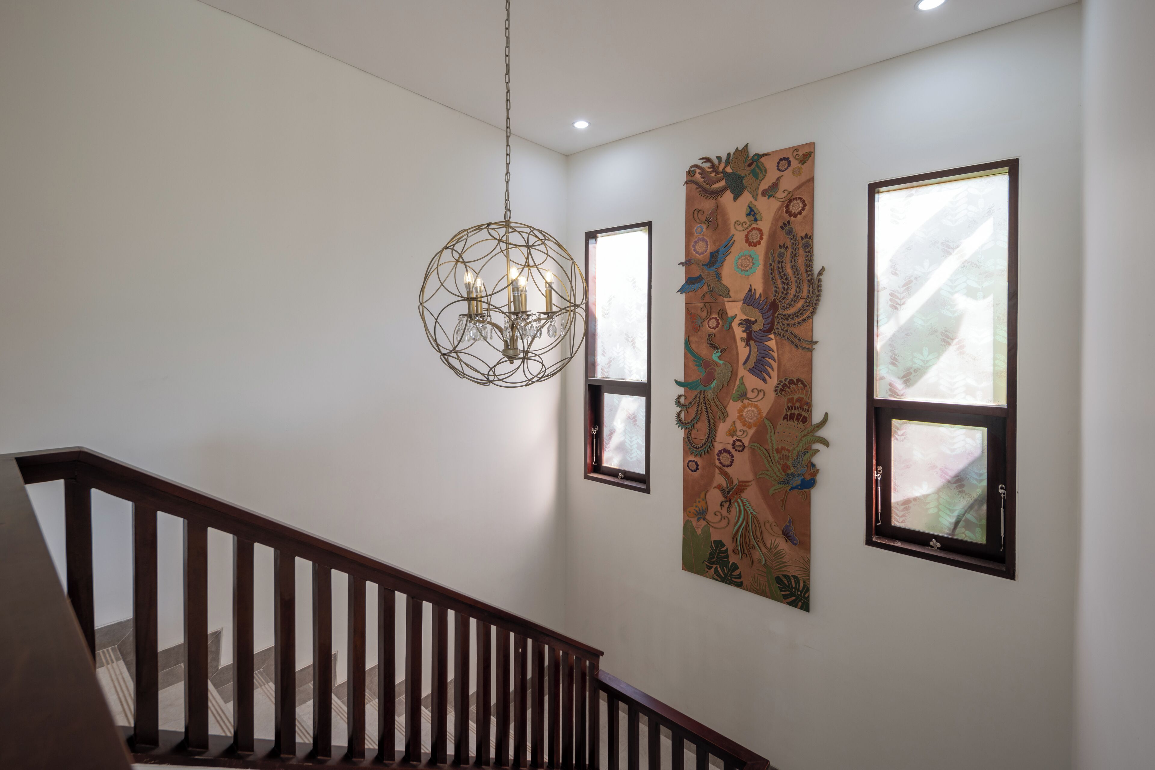 A staircase with wooden railings, a hanging chandelier, and a large decorative tapestry on the wall.