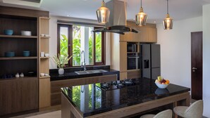 A modern kitchen with a central island, wooden cabinetry, and a large window providing natural light. - Villa UmaDahayu (Denpasar)