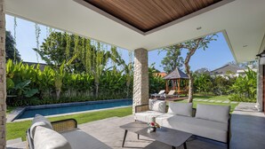 A modern outdoor patio with a pool, a stone pillar, and a seating area with a sofa and coffee table. - Villa UmaDahayu (Denpasar)