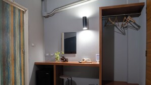 A compact room with a desk, a small stool, a trash bin, and a wooden closet with hangers. - Leisure Hostel (Krabi)