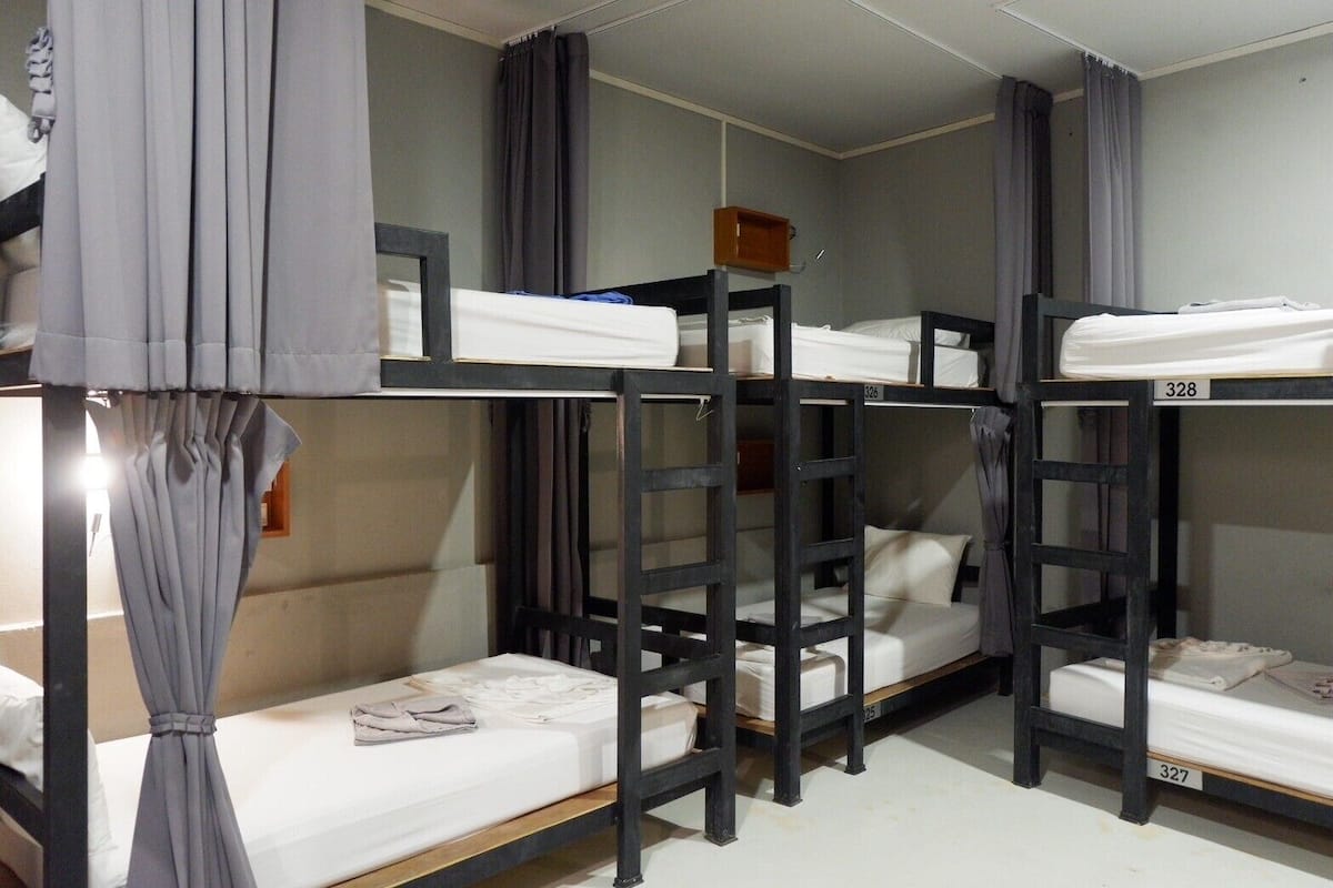 A dormitory room with bunk beds, numbered beds, and curtains.