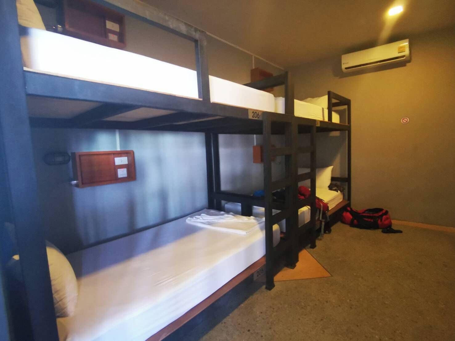 A bunk bed room with a wooden frame, a white mattress, and a red bag on the floor.